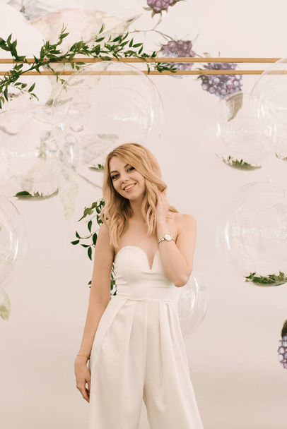 A beautiful blonde girl on the background of a photo zone with transparent bubble balls and sprigs of ruskus for an event or birthday - Fotografie, Obrázek