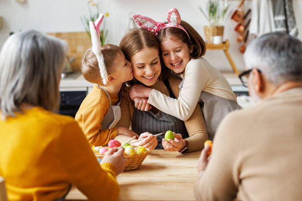 Aranyos kisgyerekek ölelkeznek és csókolóznak fiatal boldog anyával, miközben húsvéti tojásokat festenek a családdal - Fotó, kép