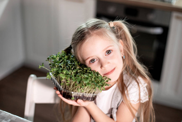 Vidám lány zöld salátát eszik otthon a konyhában. Az egészséges étel koncepciója a gyermekek számára. A gyerek - vegetáriánus. Vegán nyers étel diéta. Finom mikrozöldek gazdag vitaminok. szelektív fókusz - Fotó, kép
