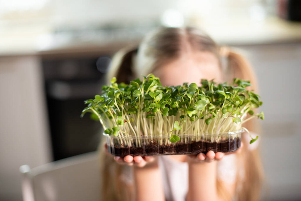 Neşeli kız evde mutfakta yeşil salata yiyor. Çocuklar için sağlıklı yiyecek kavramı. Çocuk vejetaryen. Vejetaryen çiğ gıda diyeti. Lezzetli mikro yeşiller zengin vitaminler. seçici odak - Fotoğraf, Görsel
