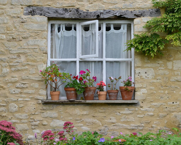Uitzicht op bloemen in potten op een traditioneel huisje venster - Foto, afbeelding