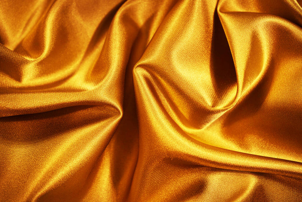 Golden silk satin. Wavy folds. Shiny surface fabric. Beautiful silky background with space for design. - Фото, зображення