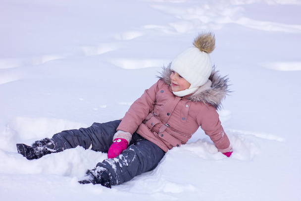 Cute little girl lies in a snowdrift and smile. Winter holiday leisure. - Fotoğraf, Görsel