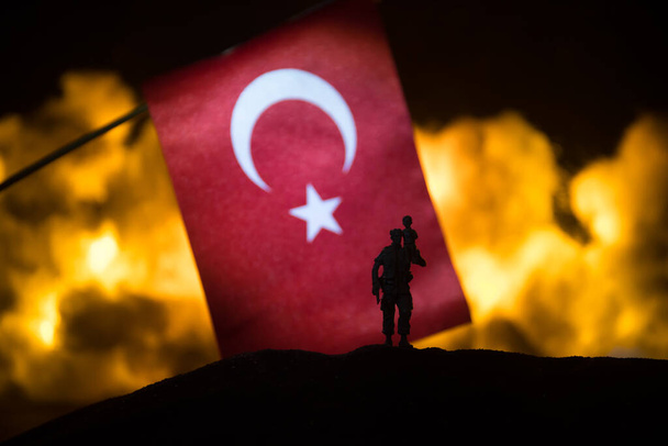 Турция небольшой флаг на горящем темном фоне. Концепция кризиса войны и политических конфликтов между народами. Силуэт вооруженного солдата против турецкого флага. Селективный фокус - Фото, изображение