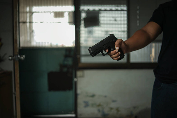 Man holding a pistol, standing in a room in black, pointing and aiming a gun at a target. concept of assassination, murder, criminal - Foto, immagini