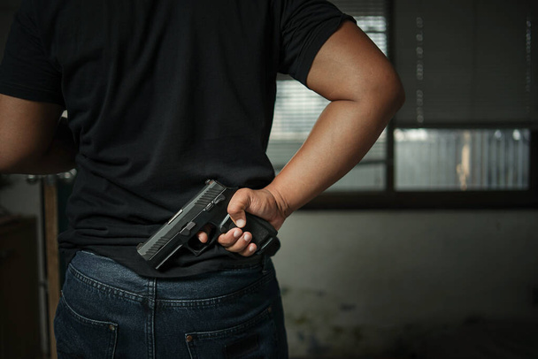 暗殺殺人犯罪者という黒の概念で後ろに立って拳銃を持っている男 - 写真・画像