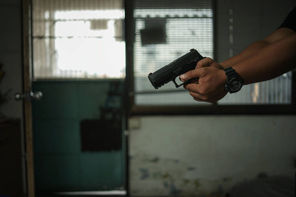 Man holding a pistol, standing in a room in black, pointing and aiming a gun at a target. concept of assassination, murder, criminal - Foto, Imagen