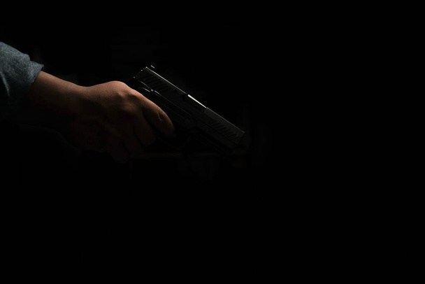Muž v modré džínové košili stojí v tmavé místnosti s pistolí. Namiř a miř na cíl. koncept atentátu, vraždy, trestného činu - Fotografie, Obrázek