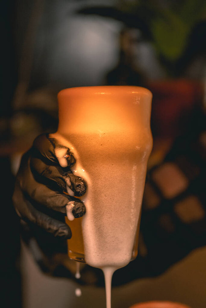 Barman mano sosteniendo un vaso de cerveza fresca espumosa ligera - Foto, imagen