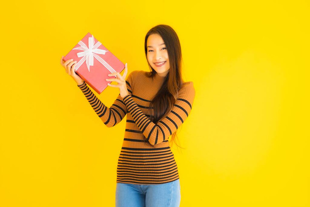 Portrait beautiful young asian woman happy smile with red gift box on yellow isolated background - Fotoğraf, Görsel