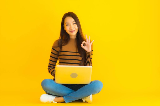 Güzel bir Asyalı kadın portresi, sarı izole edilmiş arka planda dizüstü bilgisayar kullanmak için yere oturur. - Fotoğraf, Görsel