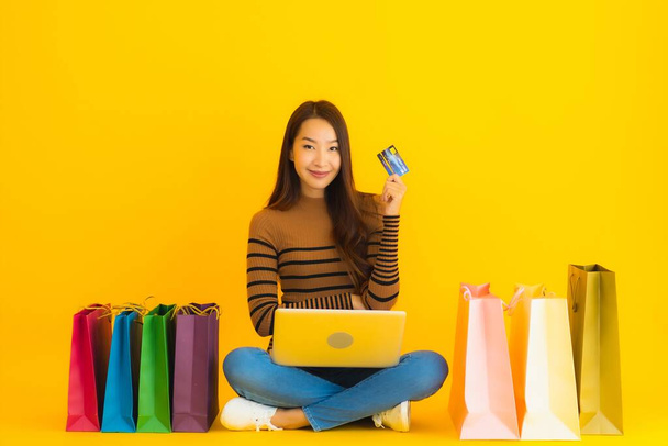 Piękny portret młoda azjatycka kobieta siedzieć na podłodze z laptopem lub komputera użyć karty kredytowej do zakupów online worek na żółtym tle - Zdjęcie, obraz