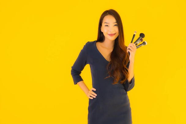 Портрет красива молода азіатка з пензлем для макіяжу на жовтому ізольованому фоні
 - Фото, зображення