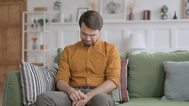 Молодой человек плачет, сидя на диване - Фото, изображение