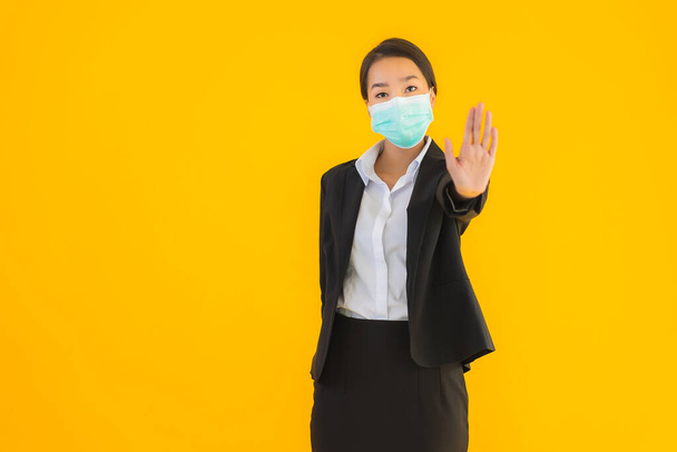 Portret mooi jong bedrijf aziatische vrouw dragen masker voor de bescherming van covid19 coronavirus op geel geïsoleerde achtergrond - Foto, afbeelding
