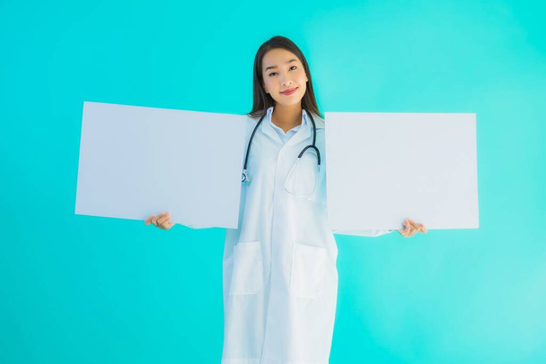 Portrait beautiful young asian doctor woman with empty card billboard banner on blue isolated background - Photo, Image