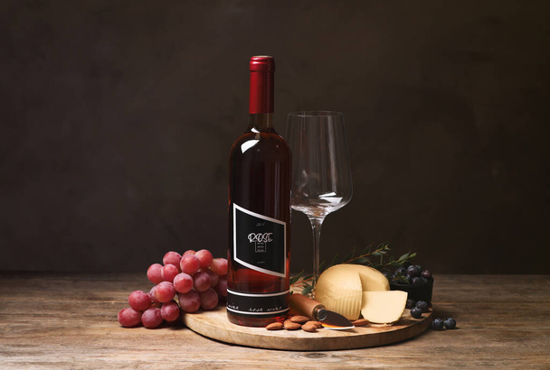 Bottle of red wine with glass and appetizers on wooden table - Foto, afbeelding