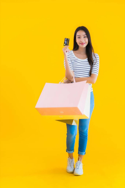 Портрет красивая молодая азиатская женщина с красочной сумки и кредитной карты на желтом изолированном фоне
 - Фото, изображение