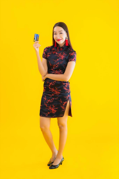 Портрет красивая молодая азиатская женщина носить китайское платье с кредитной картой и смартфон на желтом изолированном фоне
 - Фото, изображение