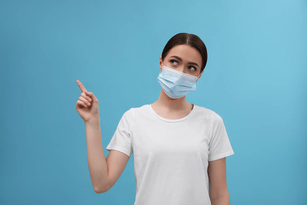 Woman in medical mask pointing at something on light blue background - Fotó, kép