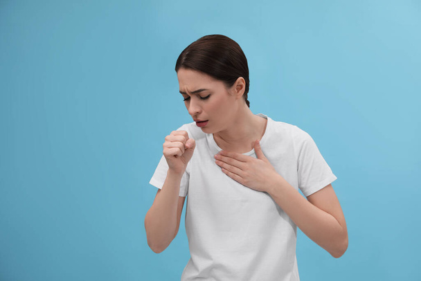 Woman coughing on light blue background. Cold symptoms - Foto, Imagem