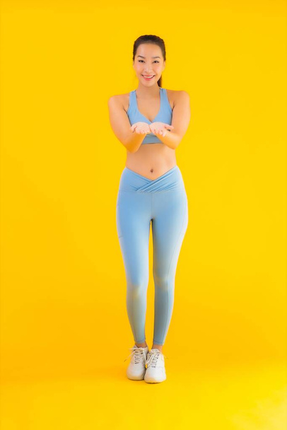 Portrét krásná mladá asijská sportovní žena se sportovním oblečením připraven k cvičení na žlutém izolovaném pozadí - Fotografie, Obrázek