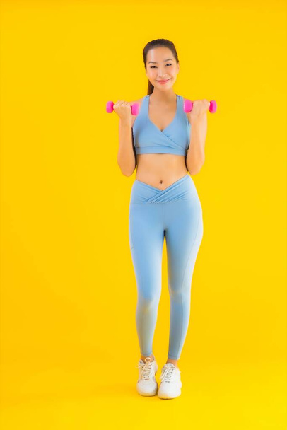 Portrait beautiful young asian woman with dumbbell and sportwear ready for exercise on yellow isolated background - Photo, Image