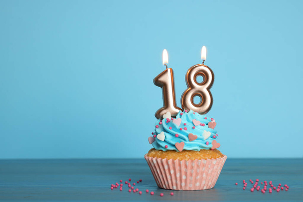 Вечеринка по случаю совершеннолетия - 18 лет. Вкусный кекс с числовой формы свечи на светло-голубом фоне, пространство для текста - Фото, изображение