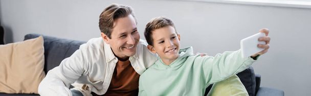Positive parent and preteen son taking selfie on smartphone at home, banner  - Foto, Imagen