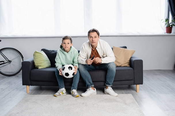 Père et garçon avec football regarder la télévision à la maison  - Photo, image
