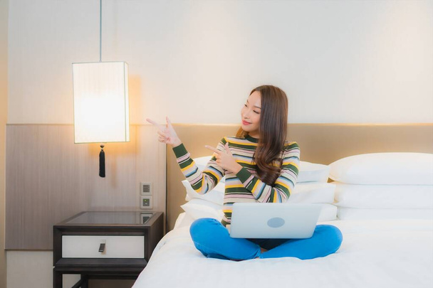 Portret mooie jonge aziatische vrouw gebruik laptop computer op bed in slaapkamer interieur - Foto, afbeelding