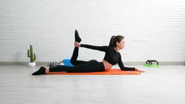 la chica lleva a cabo un entrenamiento en casa estiramiento para fortalecer su espalda - Metraje, vídeo