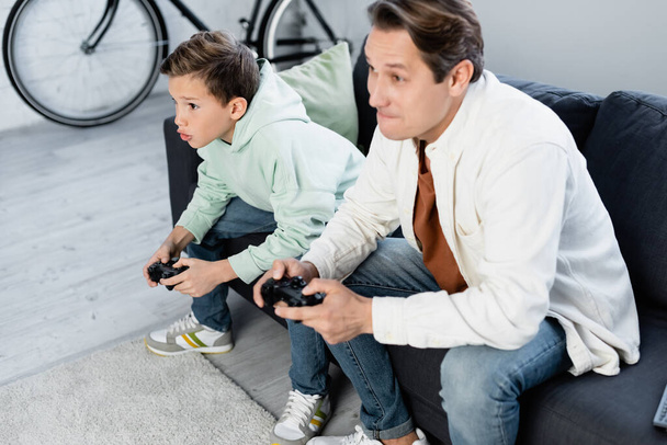 KYIV, UCRANIA - 11 de octubre de 2021: Niño enfocado jugando videojuegos con papá en casa  - Foto, imagen