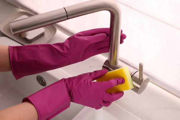 Woman in gloves cleaning faucet of kitchen sink with sponge, closeup - Φωτογραφία, εικόνα