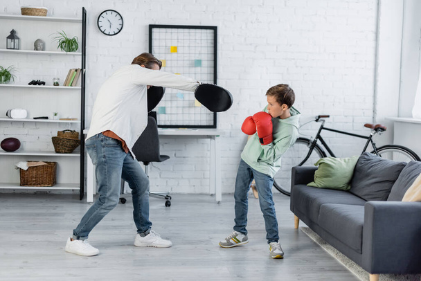 Preteen son in boxing gloves training with dad at home  - Foto, afbeelding