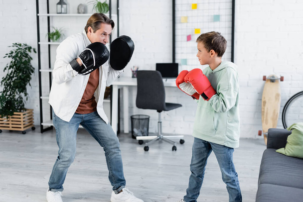 Άντρας σε punching pads κοιτάζοντας γιο πυγμαχία στο σπίτι  - Φωτογραφία, εικόνα