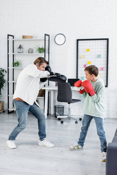 Παιδί στο μποξ γάντια εκπαίδευση με τον μπαμπά σε punching pads στο σπίτι  - Φωτογραφία, εικόνα