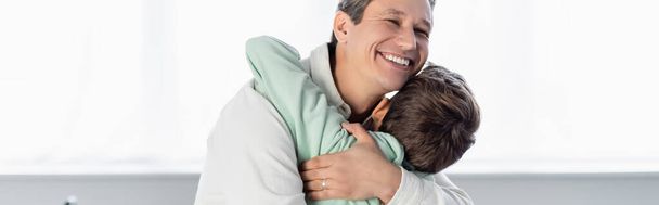 Ένας χαμογελαστός άντρας αγκαλιάζει τον γιο του στο σπίτι, σημαία  - Φωτογραφία, εικόνα
