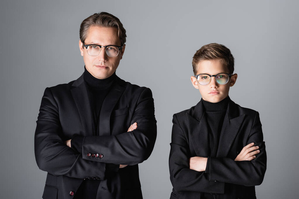 Stylish man and boy in jackets and eyeglasses crossing arms isolated on grey  - Фото, изображение