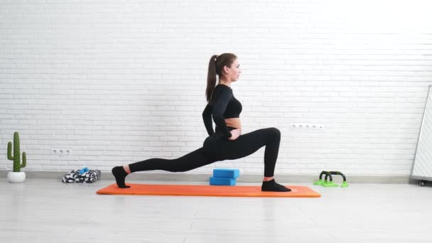 het meisje voert een home stretching workout om te zitten op de spleten doen van de lunges oefening - Video
