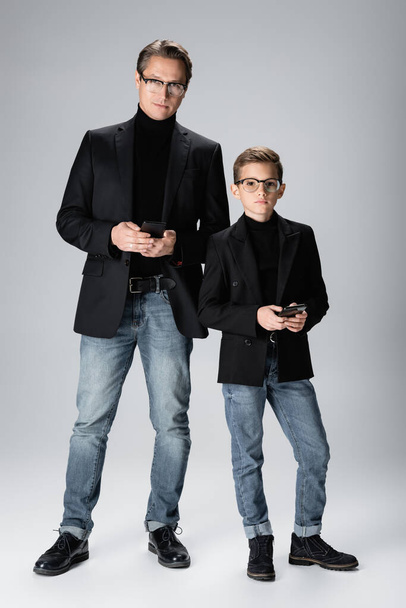 Повна довжина стильного батька і хлопчика, що тримає мобільні телефони на сірому фоні
  - Фото, зображення