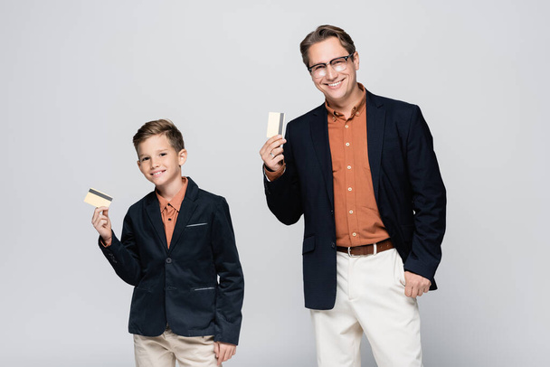 Smiling dad and son holding credit cards isolated on grey  - Foto, Bild