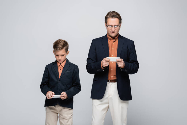 Father and son in jackets using cellphones isolated on grey  - Zdjęcie, obraz