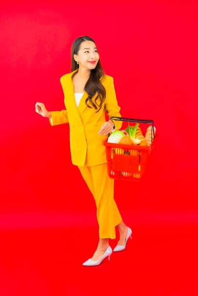 Portrait beautiful young asian woman with grocery basket from supermarket on red background - Fotó, kép