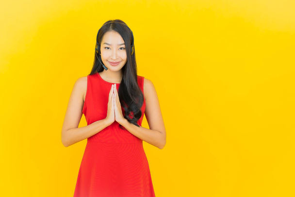 Портрет красива молода азіатка з гарнітурою для спілкування та підтримки служби колл-центру на жовтому фоні
 - Фото, зображення