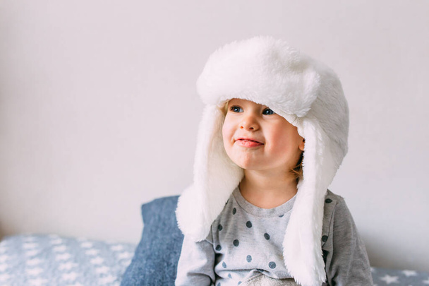 Roztomilé dítě y na posteli v útulném oblečení pro dospělé a klobouku s klapkami na uši. - Fotografie, Obrázek
