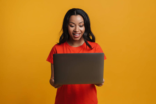 Young black woman smiling while posing with laptop isolated over yellow background - Fotografie, Obrázek