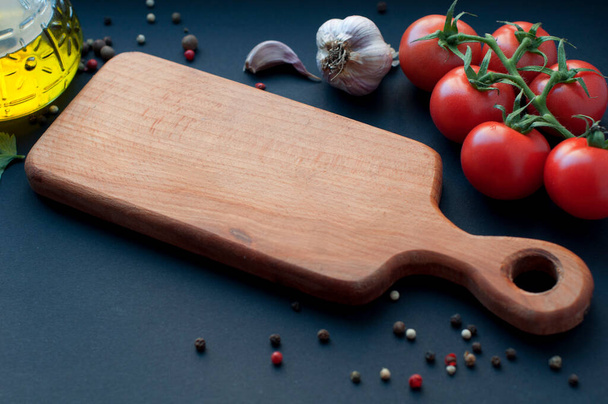 Empty wooden board with food ingredients on black background. Garlic, tomatoes, spices, pepper, parsley around wooden board - Photo, Image