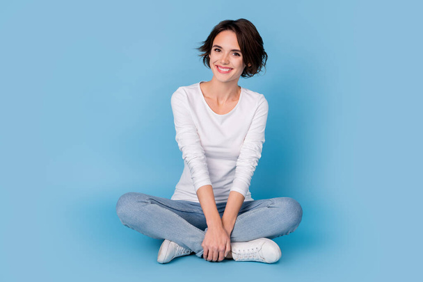 Photo of charming sweet lady dressed white shirt smiling sitting legs crossed isolated blue color background - Foto, Bild