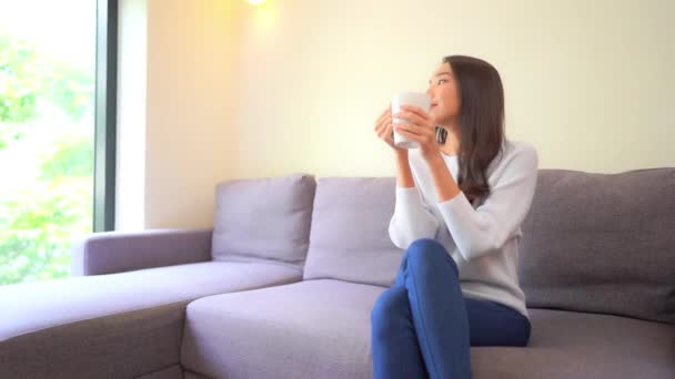 美人アジア人女性が熱い飲み物でソファでリラックスした映像 - 映像、動画